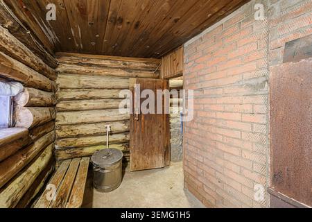 Intérieur rustique de sauna. Murs en rondins, mur de briques, plafond en bois, seau. La porte mène à une autre pièce. Sensation chaleureuse et rustique. Banque D'Images