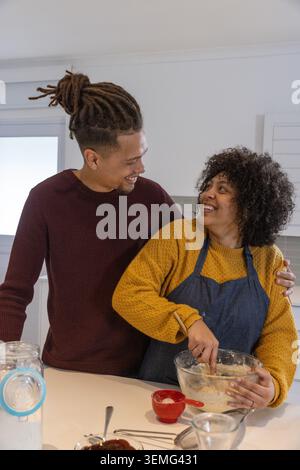 Couple afro-américain cuisson de pâte au comptoir de cuisine, bol en verre, cuillère en bois, tablier de port Banque D'Images