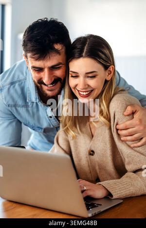 Heureux jeune diversifié, couple multiethnique budget de planification, lecture de bonnes nouvelles sur ordinateur portable à la maison Banque D'Images
