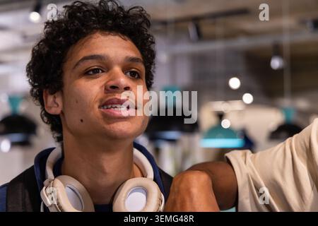 Amis adolescents debout dans un café avec un sweat à capuche sombre, un casque blanc et une sangle de sac à dos, à l'écoute Banque D'Images