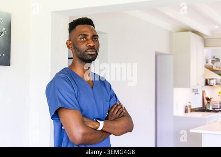 Homme africain adulte debout dans la cuisine moderne à la maison portant des gommages médicaux bleus, vérifiant smartwatch Banque D'Images