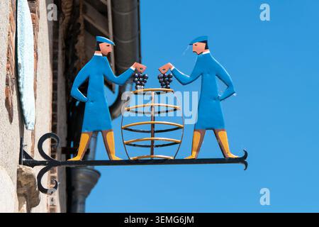 Hautvillers, France, 25 mai 2026. Panneau traditionnel en fer forgé bleu et jaune représentant deux vignerons plaçant des raisins dans un tonneau contre un Banque D'Images