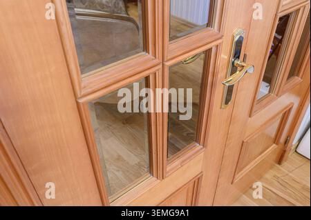 gros plan d'une porte en bois clair avec des panneaux de verre et une poignée dorée. Banque D'Images