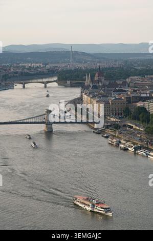 Budapest, Hongrie - 31 mai 2026 : vue verticale d'un bateau de croisière sur le Danube avec le pont des chaînes et le bâtiment du Parlement dans la soirée. Banque D'Images