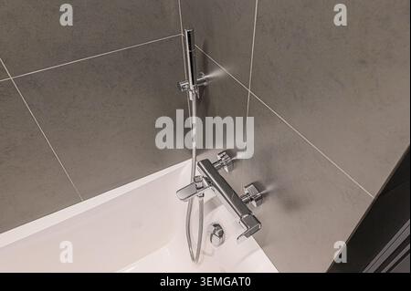 Gros plan sur une baignoire moderne avec robinet chromé et fixation de douche contre le mur carrelé gris Banque D'Images