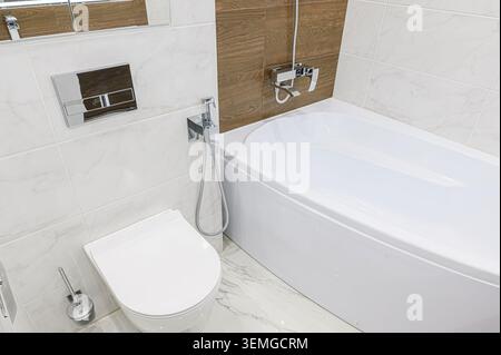 salle de bains propre avec baignoire blanche, toilettes et murs carrelés blancs et bruns. Les luminaires chromés ajoutent une touche moderne à l'espace Banque D'Images
