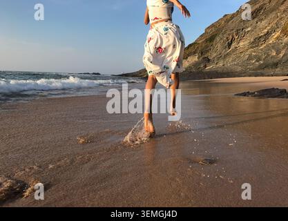 Une vue arrière forte et énergique de la moitié du corps d'une femme courir pieds nus le long d'une plage sauvage de l'océan Atlantique pendant l'heure dorée. Liberté, vitalité, aventure Banque D'Images