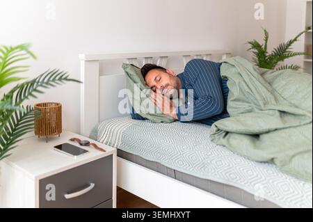 Homme dormant paisiblement sur le côté dans le lit, profitant d'une sieste bien nécessaire sous la literie verte, trouvant le confort et la détente tout en embrassant un R sain Banque D'Images