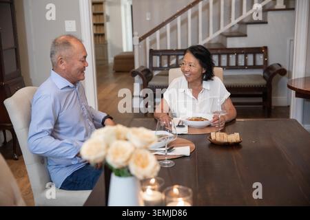 Fils matures asiatiques et mère aînée assis dans la salle à manger à la table en bois tenant le bol Banque D'Images