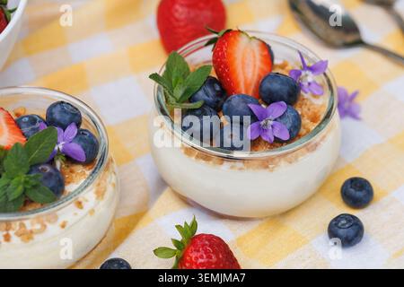 Dessert de baies fraîches dans un pot en verre avec des myrtilles, des fraises et des fleurs comestibles Banque D'Images