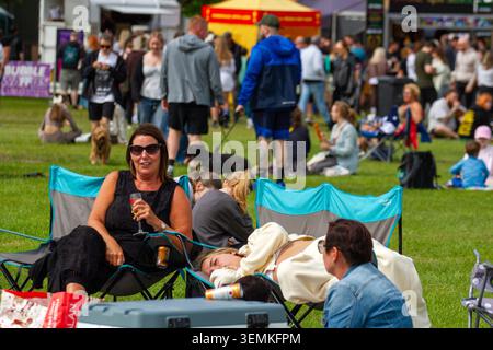 Des festivaliers se détendent dans des chaises de camping sur un champ herbeux lors d'un événement estival en plein air. Southport. Royaume-Uni Banque D'Images