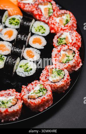Les rouleaux de sushi sont soigneusement disposés sur une plaque noire, présentant une variété de couleurs et de goûts. Le cadre est décontracté et accueillant, parfait pour un groupe d Banque D'Images