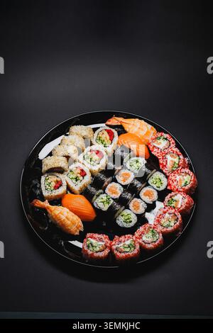 Une assiette noire ronde contient un assortiment de rouleaux de sushi et de poisson. Différents types de sushis sont soigneusement disposés, ce qui en fait un plat coloré et invitant fo Banque D'Images