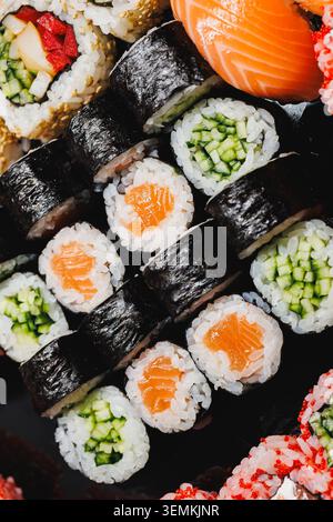Différents types de rouleaux de sushi sont placés soigneusement sur une plaque noire. Les rouleaux comprennent du saumon, du concombre et d'autres garnitures. Cette scène se produit en RES Banque D'Images