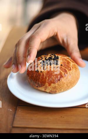 Main tend pour le pain sur une assiette blanche Banque D'Images