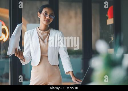 Femme d'affaires sérieuse debout avec des documents à côté de l'ordinateur portable dans la réunion de bureau, se préparant à expliquer la stratégie de projet, l'analyse commerciale et la profession Banque D'Images