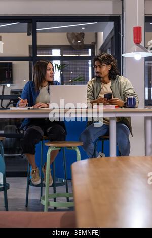 Divers collègues assis à la table commune haute dans l'espace de co-working, prenant des notes avec un ordinateur portable Banque D'Images