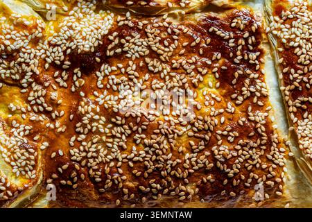 Texture de croûte de pâte feuilletée avec des graines de sésame, gros plan. Texture de fond macro de tarte cuite au four brun doré ou de croûte de pâtisserie recouverte de sésame blanc Voir Banque D'Images