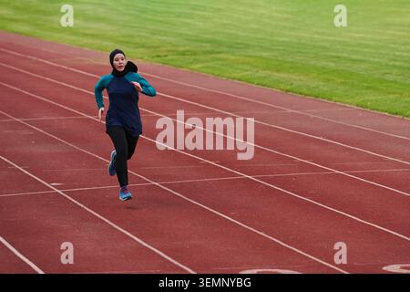 Athlète féminine qui court sur une piste extérieure portant des vêtements de sport et un foulard pendant la séance d'entraînement Banque D'Images