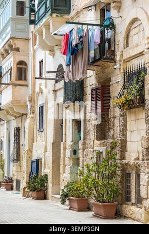 Valette, Malte — 16 mai 2025 : rue étroite traditionnelle avec des bâtiments historiques en calcaire, des balcons et une buanderie suspendue dans la vieille ville de la Valette Banque D'Images
