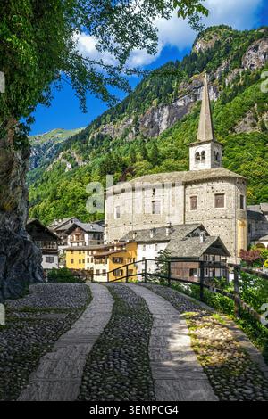 Une vue panoramique sur l'église historique en pierre et les maisons alpines traditionnelles le long d'un chemin pavé dans les montagnes verdoyantes de Campertogno, en Italie Banque D'Images