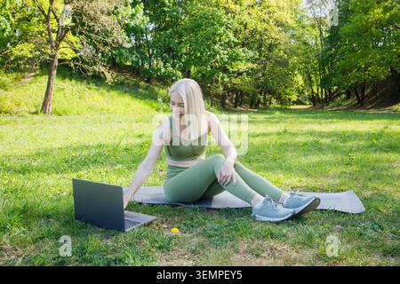 Belle femme blonde moyenne sur tapis de yoga avec ordinateur portable en été Banque D'Images