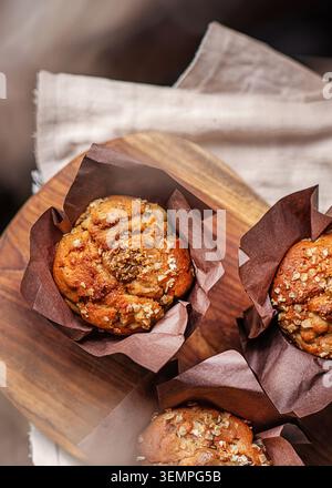 Muffins à la banane à grains entiers fraîchement cuits dans des emballages en papier tulipe brun, servis sur une planche de bois rustique avec un linge de lin. Banque D'Images