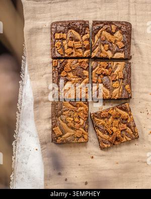 Un cliché à plat de six tranches carrées de brownie au chocolat avec un tourbillon de beurre d'arachide et des garnitures de miettes de biscuits sur un fond de lin. Banque D'Images