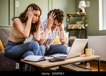 Couple examinant les finances de la maison sur ordinateur portable. Ils sont en état de choc à cause d'une dette énorme. Banque D'Images