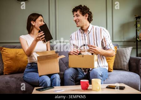 Couple adulte déballage leurs colis livrés à domicile. Ils montrent de nouveaux produits les uns aux autres. Banque D'Images