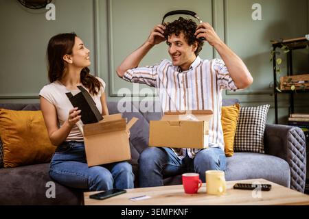 Couple adulte déballage leurs colis livrés à domicile. Ils montrent de nouveaux produits les uns aux autres. Banque D'Images