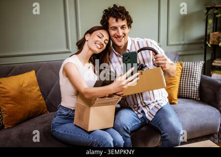 Couple adulte déballage leurs colis livrés à domicile. Ils prennent selfie avec de nouveaux objets. Banque D'Images