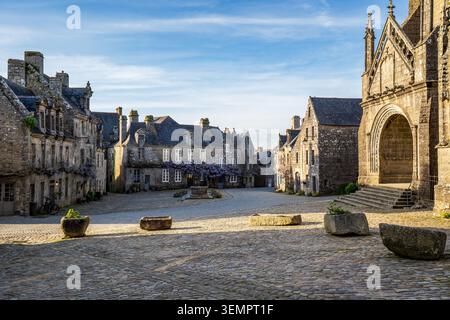 Une vue large de la place historique de Locronan, Bretagne, montrant le pavé ensoleillé, les anciennes jardinières en pierre au premier plan, la tradition Banque D'Images