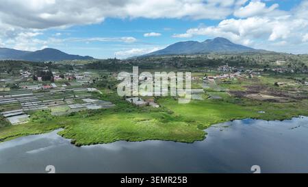 Vue aérienne d'Alahan Panjang avec des champs agricoles et un lac calme sous un ciel nuageux à Lembah Gumanti, Sumatra Ouest, Indonésie. Banque D'Images