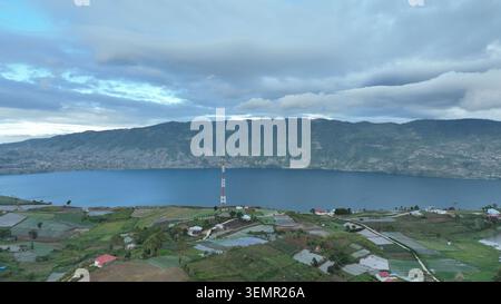 Vue aérienne d'Alahan Panjang avec une tour de télécommunications surplombant les eaux bleues du lac Diatas et les champs agricoles luxuriants à Lembah G. Banque D'Images
