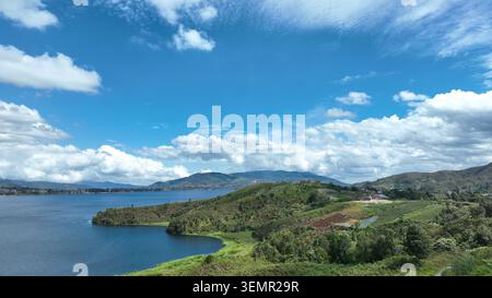 Vue aérienne d'Alahan Panjang avec un vaste lac bleu entouré de collines verdoyantes et un ciel nuageux lumineux à Lembah Gumanti, Sumatra Ouest, Indon Banque D'Images
