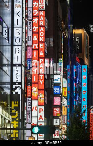 Vue en bas angle d'étroites enseignes de gratte-ciel d'entreprise éclairées au néon le long d'une rue animée de quartier de divertissement, Shinjuku, Tokyo, Japon Banque D'Images