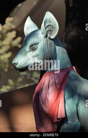 Vue rapprochée d'une statue de renard en pierre portant un bavoir rouge dans un sanctuaire shinto, Tokyo, Japon Banque D'Images