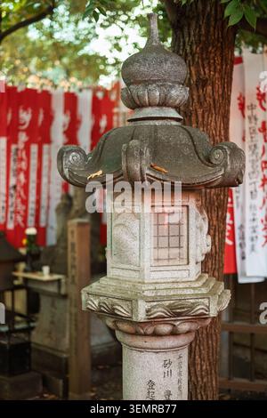 Pilier de lanterne en pierre traditionnel debout à l'extérieur à côté des bannières de prière blanches et rouges suspendues dans un sanctuaire, Tokyo, Japon Banque D'Images