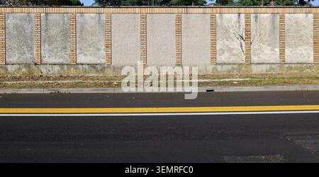 Mur en ciment brut et briques. Trottoir herbeux et rue avec des lignes de démarcation de circulation jaunes et blanches. Arrière-plan de l'espace de copie. Banque D'Images