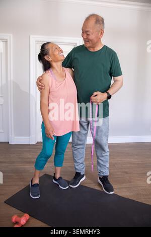 Couple chinois asiatique debout sur un tapis noir à la maison, tenant du ruban rose et portant des vêtements d'entraînement Banque D'Images