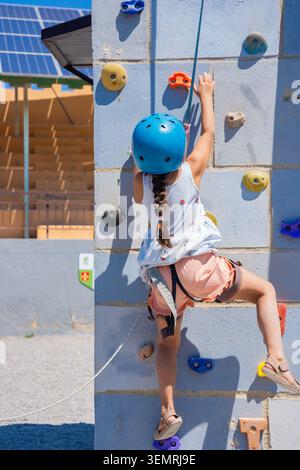 Enfant grimpant mur extérieur coloré avec équipement de sécurité en plein soleil Banque D'Images