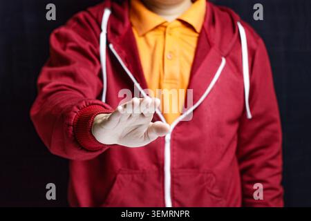Homme dans le sweat à capuche rouge faisant Stop Hand Gesture sur fond sombre. Montrant un geste d'arrêt de paume, symbolisant le déni, le refus, les frontières personnelles, le rejet, ou arrêter une action. Photo de haute qualité Banque D'Images