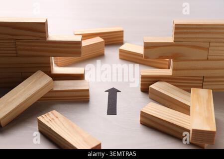 Mur en bois effondré fait de blocs et flèche de papier sur la table, gros plan. Surmonter les obstacles Banque D'Images