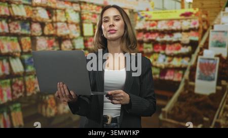 Une femme tient un ordinateur portable et scanne les étagères des paquets de semences tout en vérifiant les niveaux de stock dans l'immeuble ; planification de la vente au détail en toute confiance. Banque D'Images