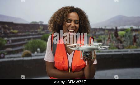 Femme technicienne souriante et tenant un drone tout en portant un gilet de sécurité orange dans la rue ; expertise en innovation de confiance. Banque D'Images