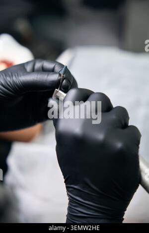Un homme adulte portant des gants noirs prépare méticuleusement un implant dentaire dans un cabinet dentaire stérile. Ambiance professionnelle et attentionnée reflète Preci Banque D'Images
