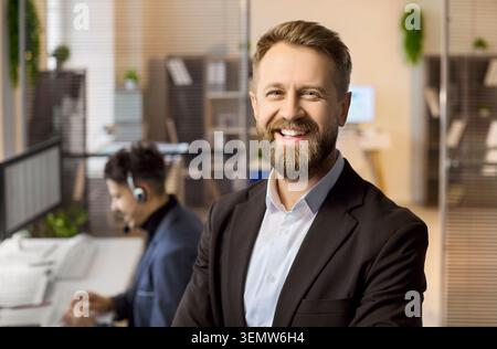 Portrait de gestionnaire d'homme d'affaires souriant dans un bureau moderne avec un collègue aux ordinateurs Banque D'Images