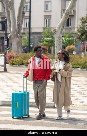 Heureux marié afro-américain homme et femme souriant et parlant tout en marchant dans la rue Banque D'Images