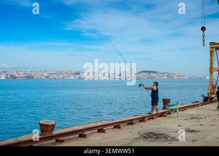 LISBONNE, PORTUGAL - nov 09, 2025 : homme pêchant depuis la jetée de Cais do Sodre sur le Tage, Lisbonne skyline en arrière-plan. Banque D'Images